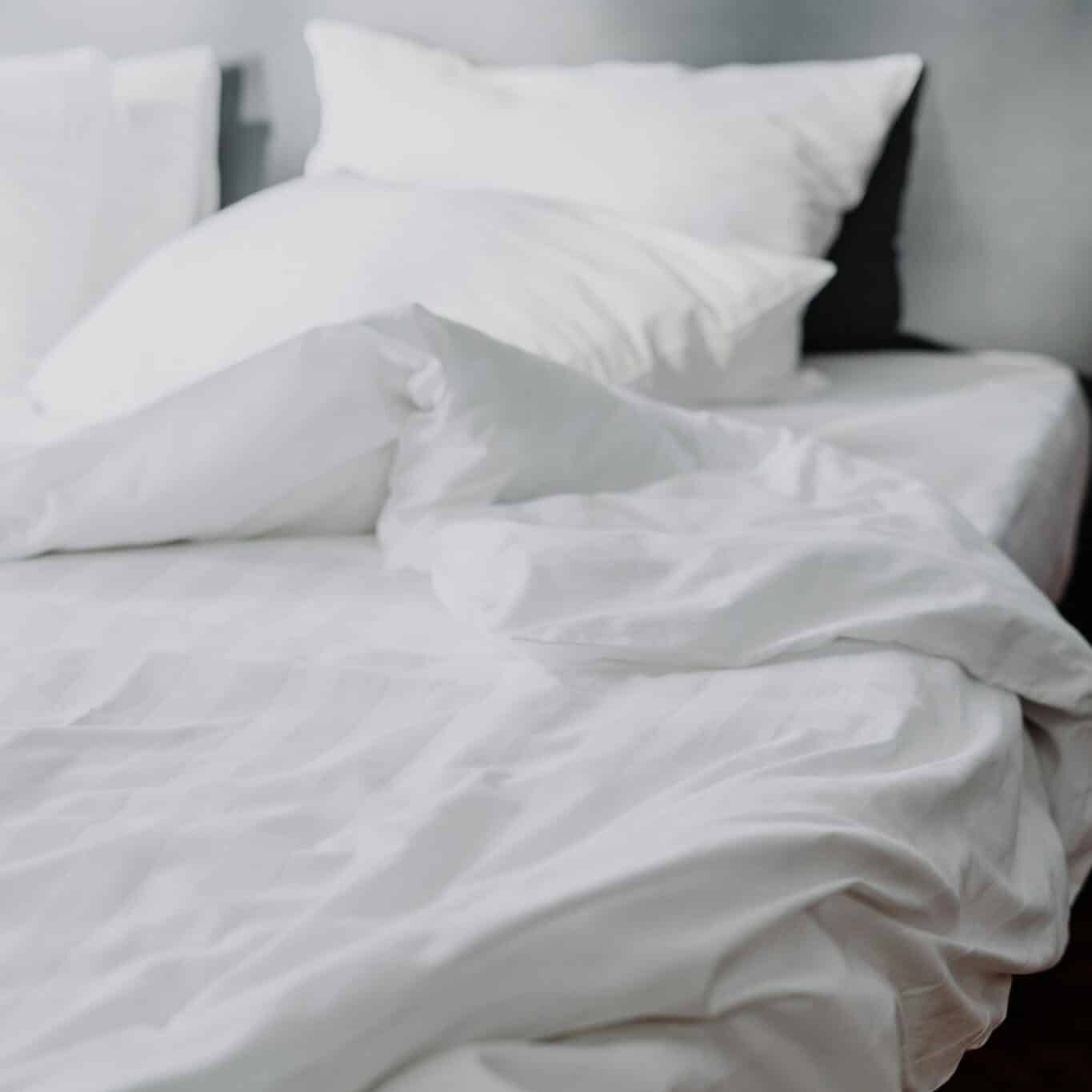 A close-up of a cozy white linen bed with rumpled bedding in a modern bedroom setting.